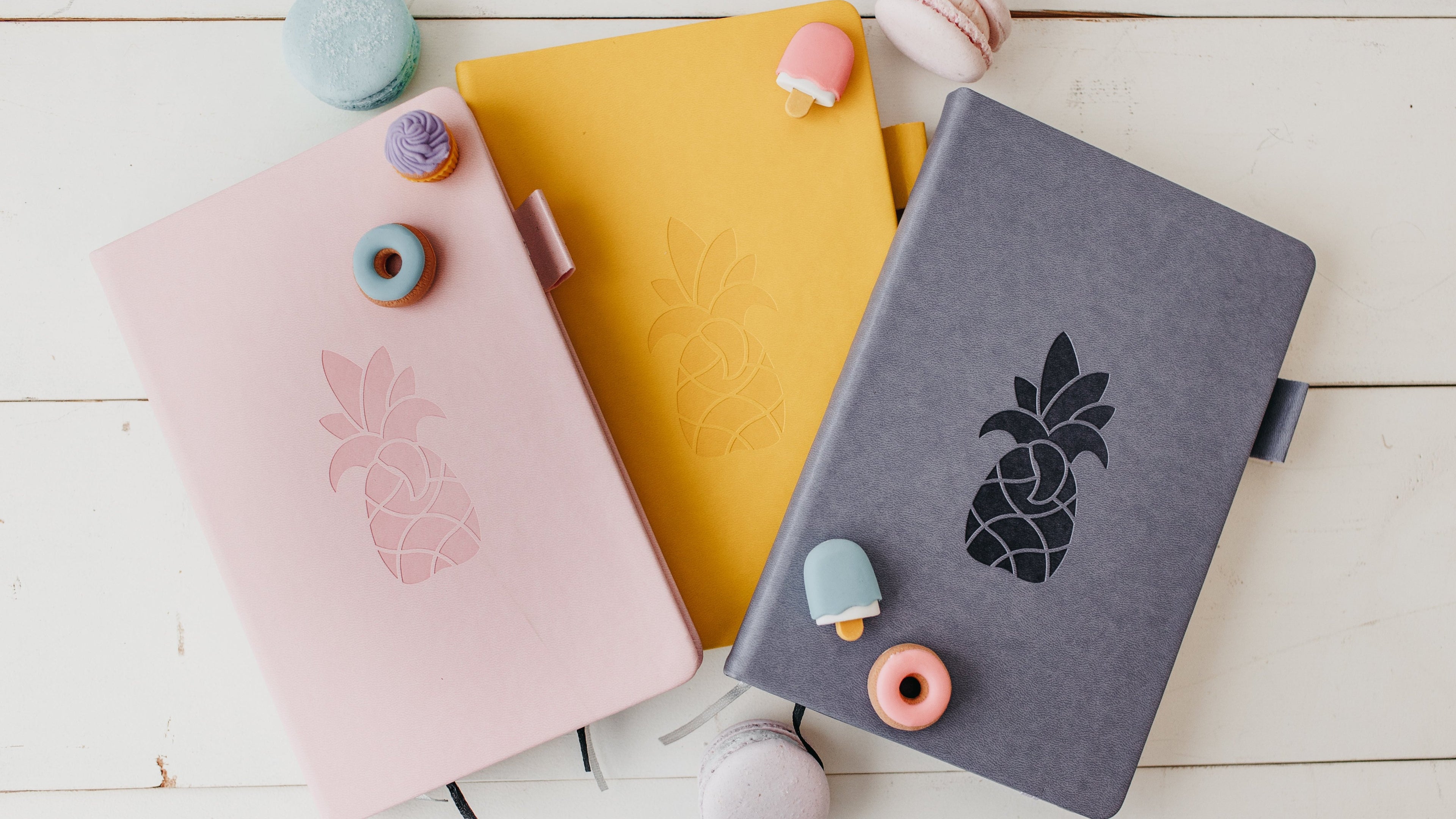 Pink, Yellow and Grey planners laying on table with candies and cookies surrounding them. 